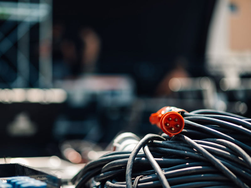 A close-up of a coiled bundle of black cables with a prominent orange-red multi-pin connector in sharp focus, set against a heavily blurred dark industrial background.